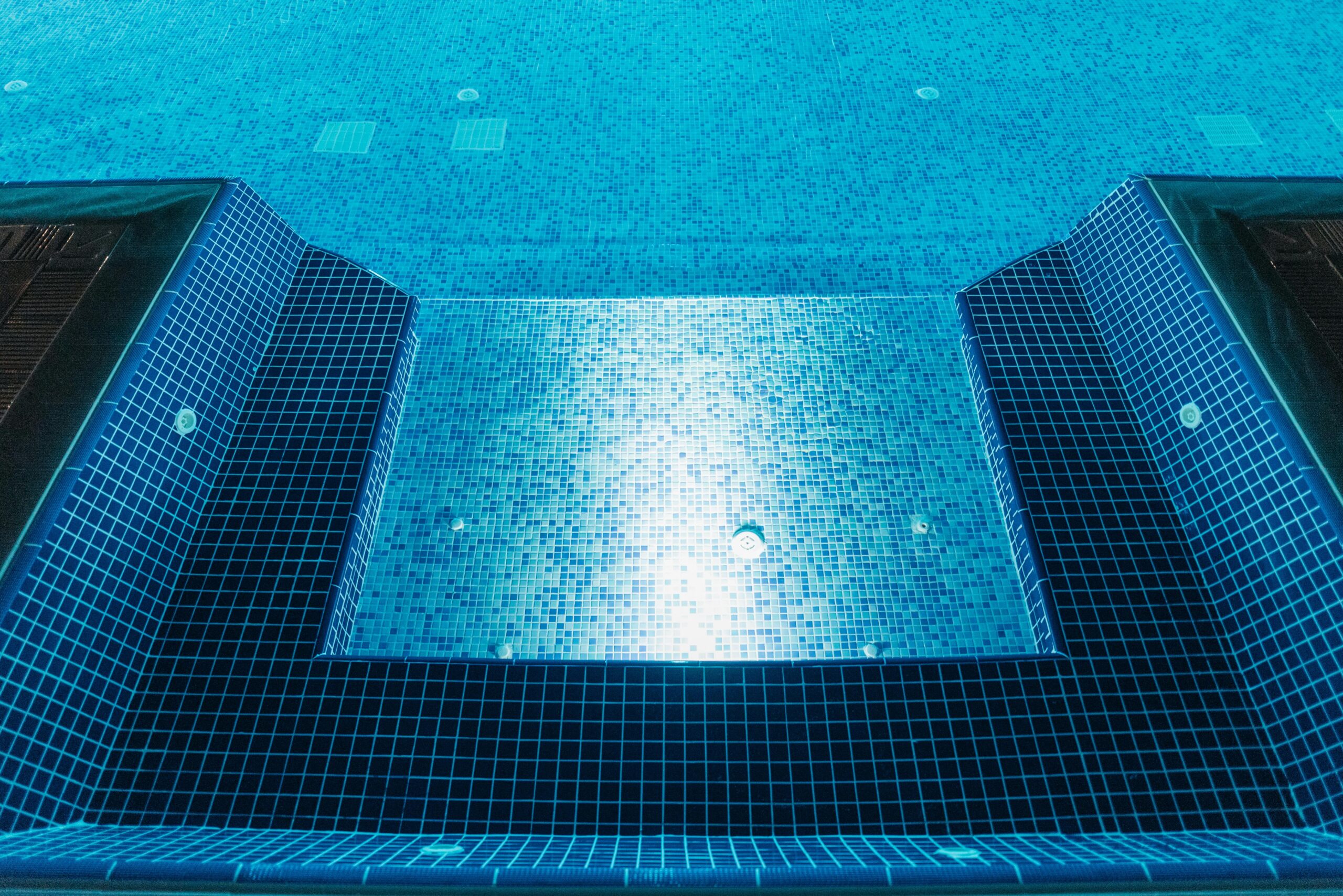 A clear view of an illuminated swimming pool with blue mosaic tiles, perfect for summer relaxation.